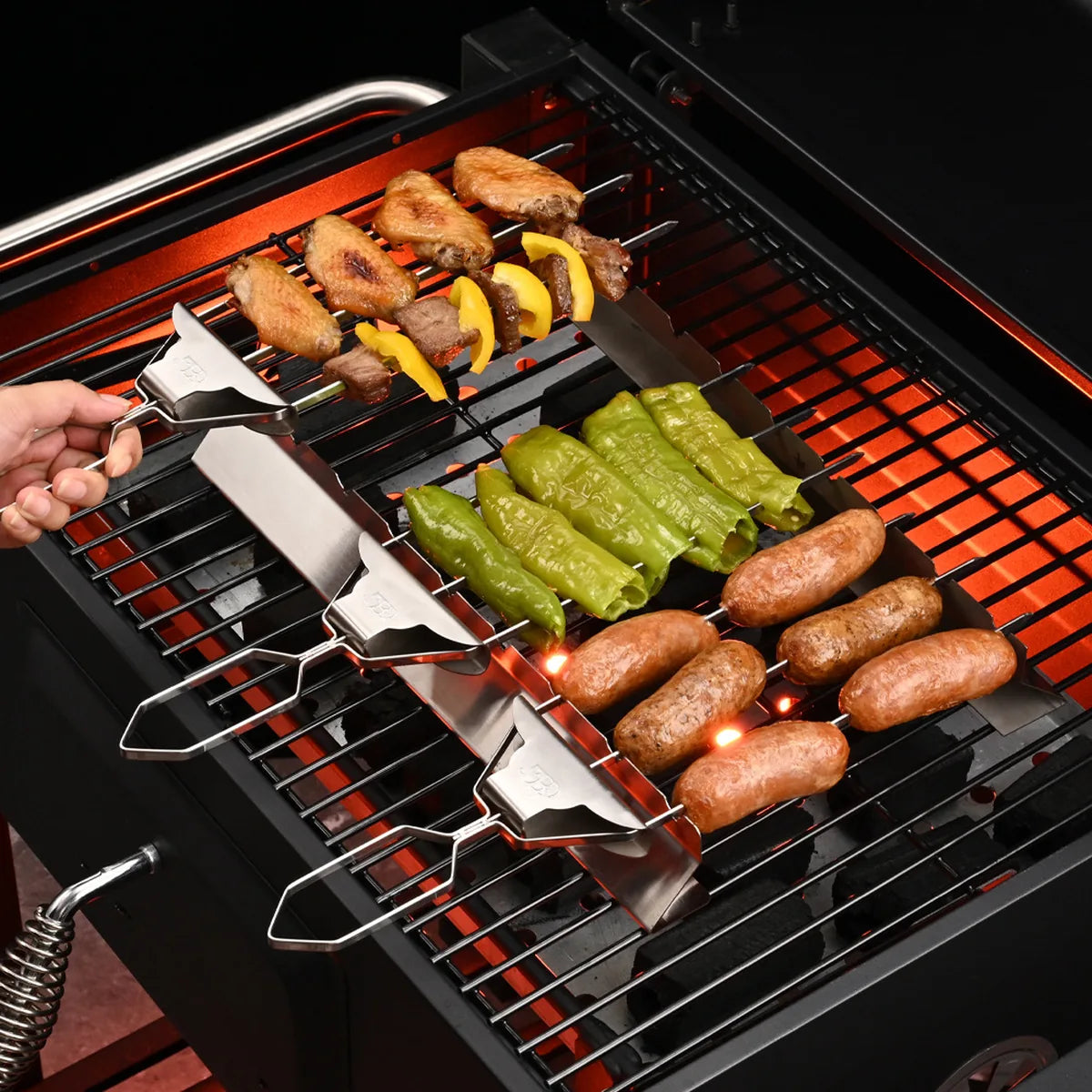 Three original three-prong BBQ skewers cooking meat, peppers, and sausages on an outdoor grill